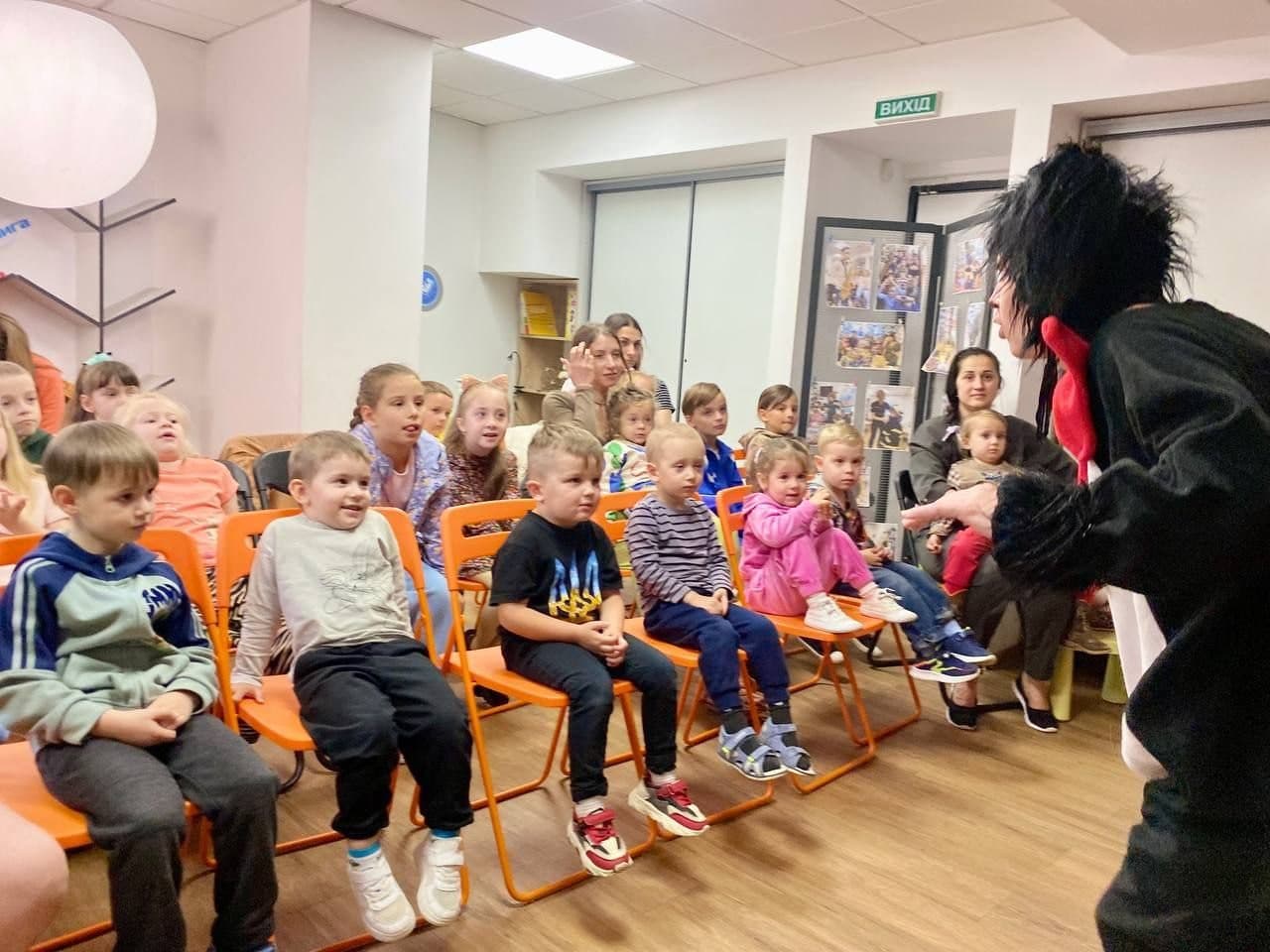 A costumed performer engages a room of seated children watching attentively.