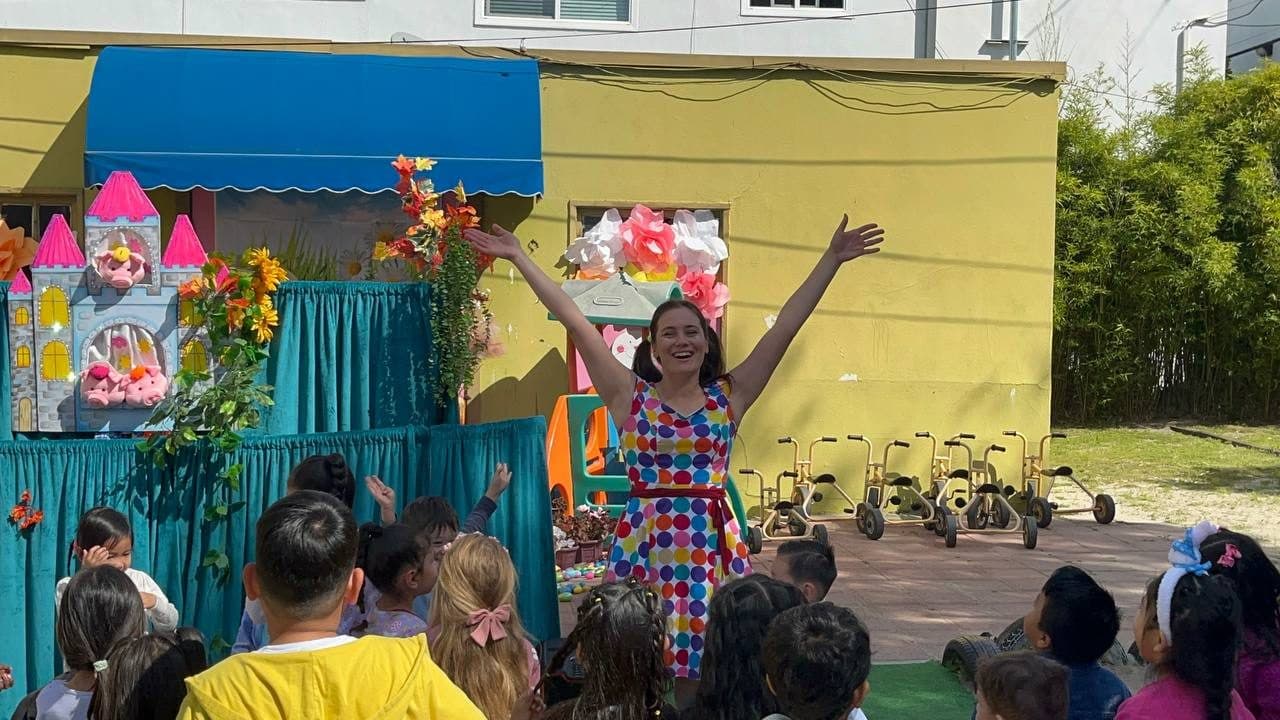 A performer throws her arms wide with joy on stage as children watch.
