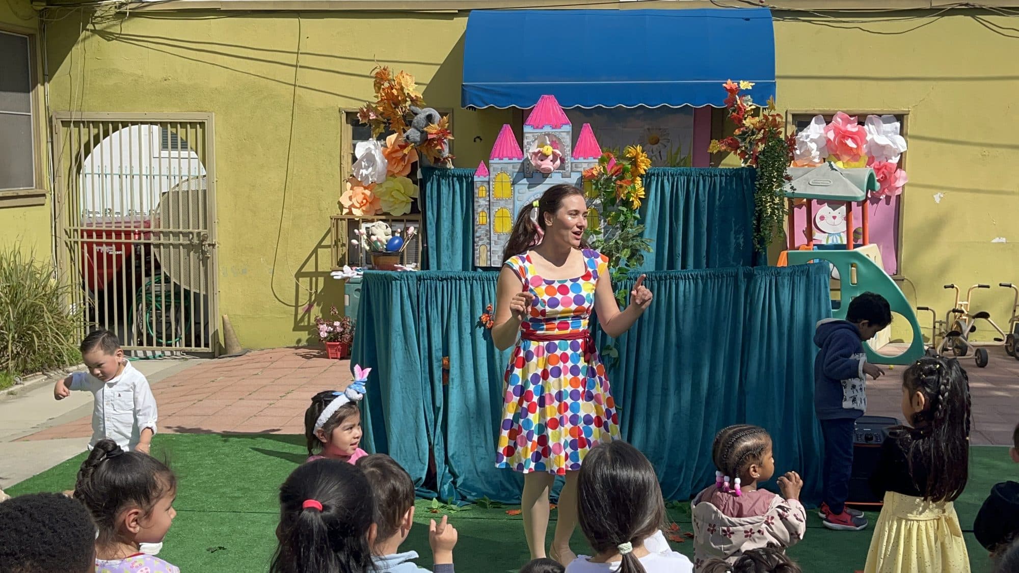 A costumed performer entertains a seated group of preschoolers in front of a colourful castle stage set.
